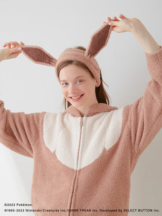 Person wearing unisex baby Moco Eevee hair band with Pokémon Sleep themed outfit, smiling and posing with raised hands like ears.