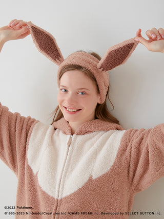 Person wearing a Pokémon-themed Eevee hair band and matching cozy outfit, smiling and holding up Eevee ears playfully.