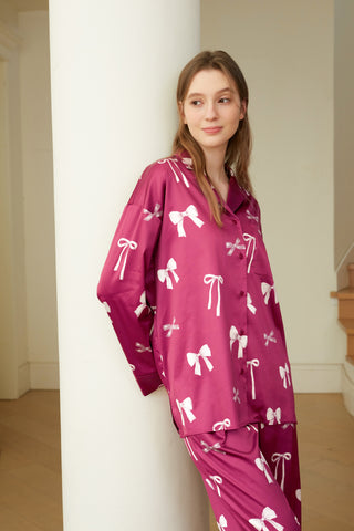 Woman wearing pink ribbon print shirt and pants set with relaxed fit and notched collar, standing against a white column indoors.