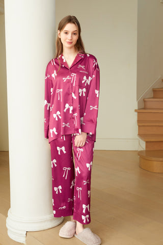 Woman wearing a pink ribbon shirt and long pants set with notched collar and button closure, standing in a modern interior.