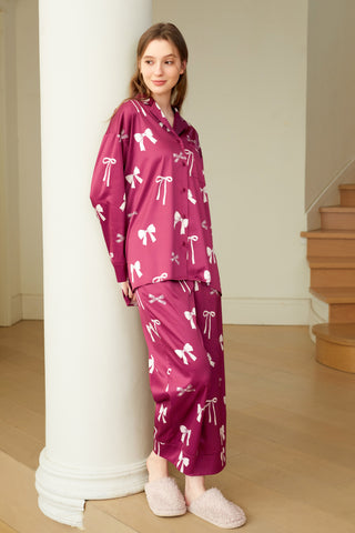 Woman wearing a silky ribbon print shirt and pants set in pink, standing by a column, showcasing stylish comfort and femininity.