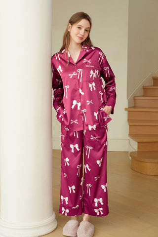 Woman wearing a pink ribbon print shirt and long pants set with a notched collar and chest pocket, standing near a staircase.