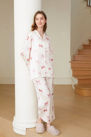 Model wearing Ribbon Shirt & Long Pants Set with pink ribbon print, relaxed fit, and notched collar, leaning against a white pillar indoors.