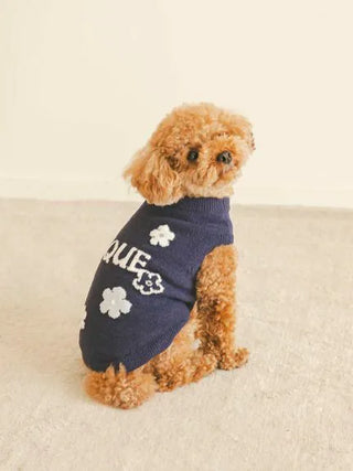 Small dog wearing a CAT&DOG Flower Logo Jacquard Pullover in navy with white flower patterns, seated on a beige carpet.
