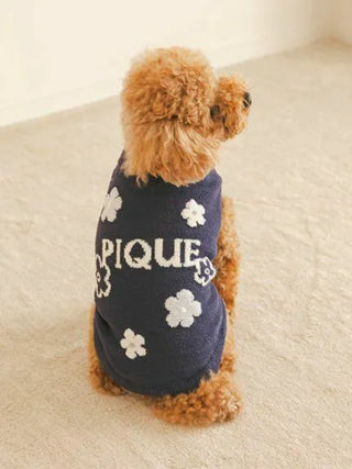Dog wearing navy CAT&DOG flower logo jacquard pullover sitting on beige carpet.