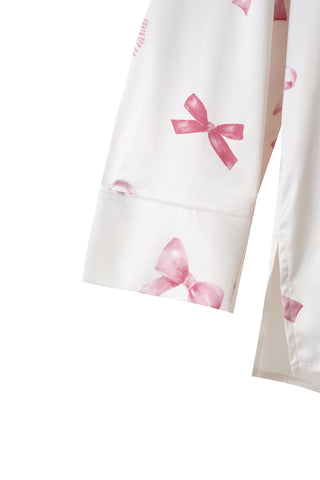 Close-up of white fabric with pink ribbon print from a Ribbon Shirt & Long Pants Set, showcasing silky texture and charming design.