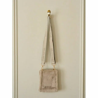 Gelato Pique Faux Fur Mini Sling Bag in beige hanging on a wall, featuring eco-friendly faux fur and branded strap.