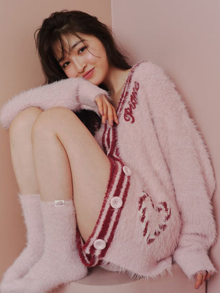 Woman wearing cozy pink feather-textured cardigan and shorts loungewear set, seated against a pastel background, smiling gently.