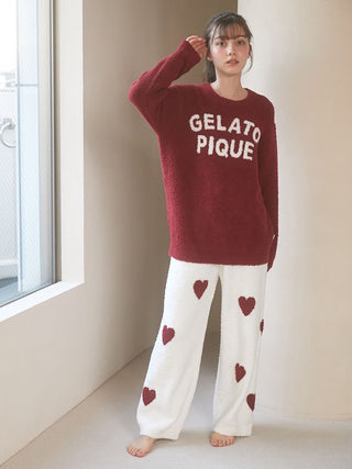 Woman wearing red Gelato Pique logo sweater and white heart-patterned pants in a cozy indoor setting.
