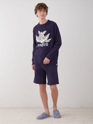 Man wearing navy pullover sweater and matching shorts with a white design, standing against a neutral background.