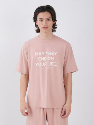 Man wearing Sarafree Logo Men's Loungewear Set with 'May They Enrich Your Life' printed on pink shirt, standing against white background.