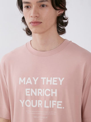 Man wearing a pink t-shirt with the text 'May They Enrich Your Life,' facing forward with a neutral expression.