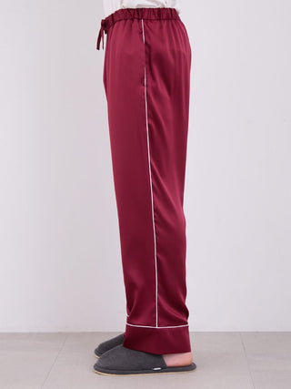 Side view of men's burgundy satin pajama pants with white piping, showcasing luxurious silky fabric for comfortable nights.