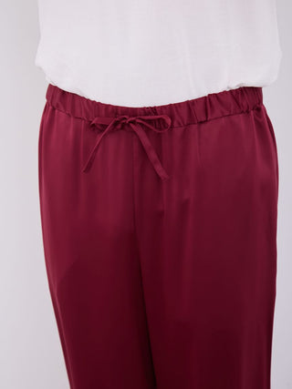Men's burgundy satin pajama pants with white piping detail, featuring a drawstring waistband for a comfortable fit.