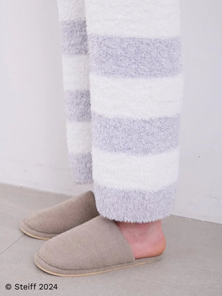 Man wearing Steiff Gelato Border Fuzzy Pajama Pants with stripe pattern, paired with slippers on a tile floor