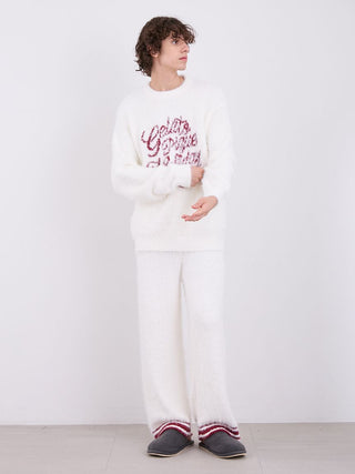 Man wearing Feather Pajama Pants and sweater standing against a white background.