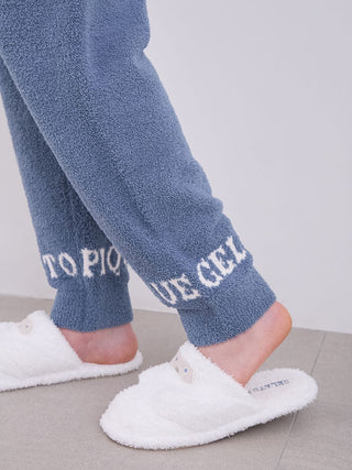 Close-up of men's blue Powder Logo Pajama Pants with "Gelato Pique" logo at cuffs, paired with white fluffy slippers.