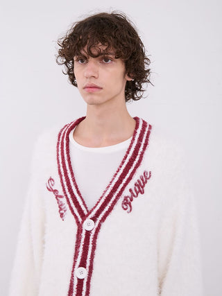 Close-up of a man wearing a white cardigan with red stripes and embroidered text on buttons, highlighting cozy and stylish design details.