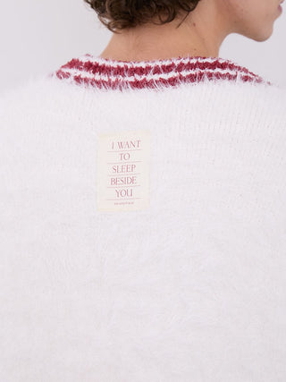 Close-up of a white fuzzy cardigan with a red-striped collar and a patch reading 'I WANT TO SLEEP BESIDE YOU' on the back.