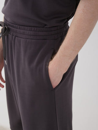 Close-up of unisex loungewear shorts with logo waistband and pocket, showcasing comfortable and stylish design in dark fabric.