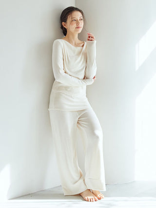 Woman wearing Snow High-Waisted Lounge Pants, ultra-soft and elegant, standing by a sunlit wall, showcasing relaxed loungewear style.