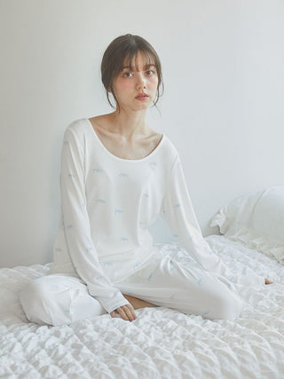 Woman wearing Motif 3-Pattern Long Sleeve T-Shirt in white, seated on bed in airy room, showcasing elegant design and soft fabric.