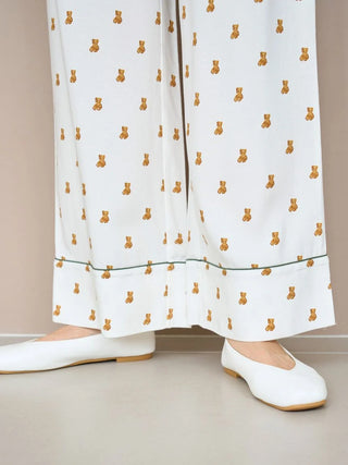 Close-up of white pajama pants with teddy bear print and white shoes, showcasing cozy, stylish bedtime or lounging attire.