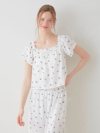 Woman wearing Gelato Pique's Floral Print Smocked Crop Top with delightful blue daisies on white, showcasing fresh and feminine style.