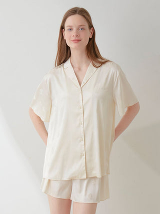 Woman wearing a cream satin pajama sleep shirt with a floral pattern, standing in a well-lit room.