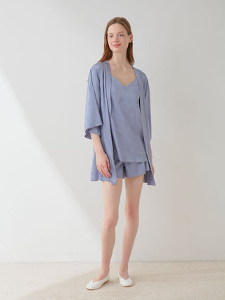 Model wearing a light blue satin long sleeve tie nightgown robe with floral pattern, standing in a minimalist setting.