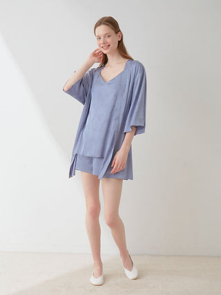 Woman wearing a blue satin nightgown and robe set, standing against a white background, smiling.