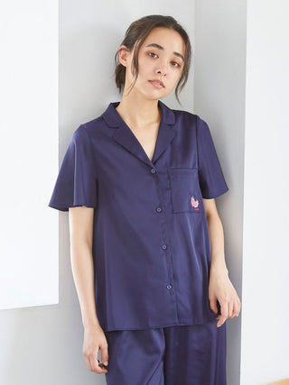 Woman wearing a navy satin sleep shirt with strawberry embroidery, button-up design, short sleeves, and luxurious feel.