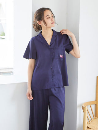 Woman wearing a navy blue satin sleep shirt with strawberry embroidery and matching pants, standing indoors.