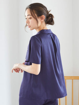 Woman wearing a navy satin sleep shirt with strawberry embroidery, showcasing the back design in a soft-lit room.