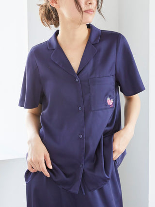 Woman wearing a navy satin button-up sleep shirt with strawberry embroidery on the pocket, showcasing comfort and style.