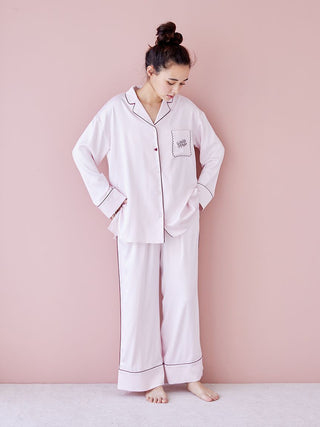 Woman wearing a piping satin long sleeve pajama shirt in pink, with elegant piping details, standing against a soft pink background.
