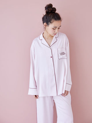 Woman wearing pink satin long sleeve pajama shirt with elegant piping detail, standing against a pink background.