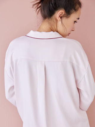 Back view of a piping satin long sleeve pajama shirt in light pink with elegant collar detail, shown on a woman in a relaxed pose.