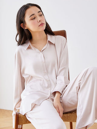 Woman wearing an elegant long sleeve satin sleepwear blouse, sitting peacefully in a chair, showcasing comfort and style.