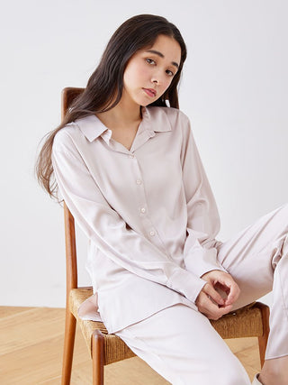 Woman wearing long sleeve satin sleepwear blouse with button-up design, seated on a chair.