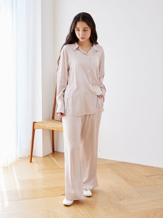 Woman wearing a long sleeve satin sleepwear blouse with a classic button-up design and pointed collar, standing in a bright room.