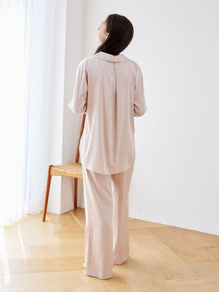 Woman wearing a long sleeve satin sleepwear blouse in a relaxed fit, showcasing the back design in a softly lit room.