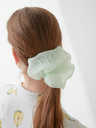 Woman wearing a sheer green hair scrunchie with embroidered 'PIQUE' letters by Gelato Pique, showcasing elegance and style.