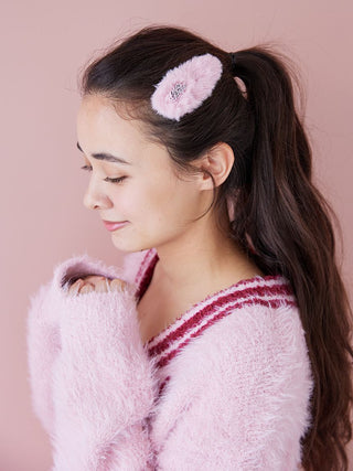 Woman wearing Gelato Pique's pink faux fur hairpin with logo, styled elegantly in her brunette hair, against a soft pink background.
