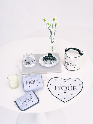 Elegant heart-patterned "Pique" satin pouches and accessories on white background, showcasing chic and sophisticated design.