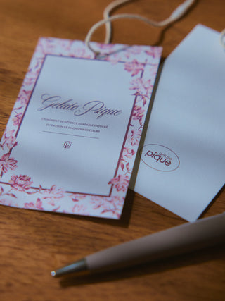Gelato Pique USA product tag with floral border on wood surface, next to pen.