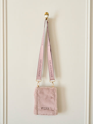 Plush faux fur mini sling bag with Gelato Pique branding and adjustable strap, hanging on a white wall.