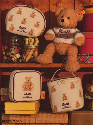 Steiff plush toy with Gelato Pique USA bags showcasing timeless quality and irresistible cuteness on a wooden shelf.