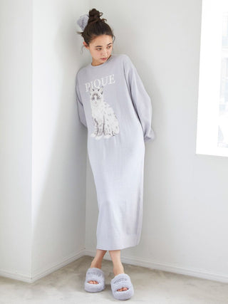 Woman wearing a long gray dress with a graphic design and Gelato Pique Eco Fur Fuzzy Slippers in a cozy room.