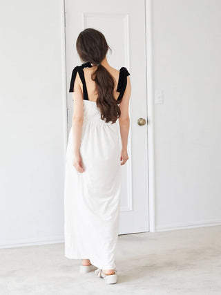 Woman in elegant white dress with black bow accents standing indoors